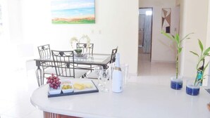 Een eethoek met een tafel gedekt voor twee personen, een plafondventilator, een schilderij en een uitzicht op een andere kamer.