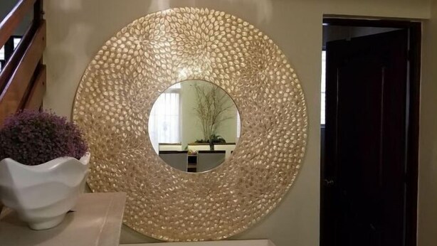 A round mirror with a textured surface on a wall, a white vase with purple flowers, and a small table with a bicycle model. - Gorgeous House in the Center of Santiago (Santiago De Los Caballeros)