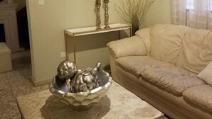 A living room with a beige sofa, a painting of a landscape, a table with a decorative bowl, and a staircase in the background. - Gorgeous House in the Center of Santiago (Santiago De Los Caballeros)