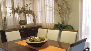A dining table with a bowl of fruit, surrounded by chairs, in a room with large windows and curtains. - Gorgeous House in the Center of Santiago (Santiago De Los Caballeros)