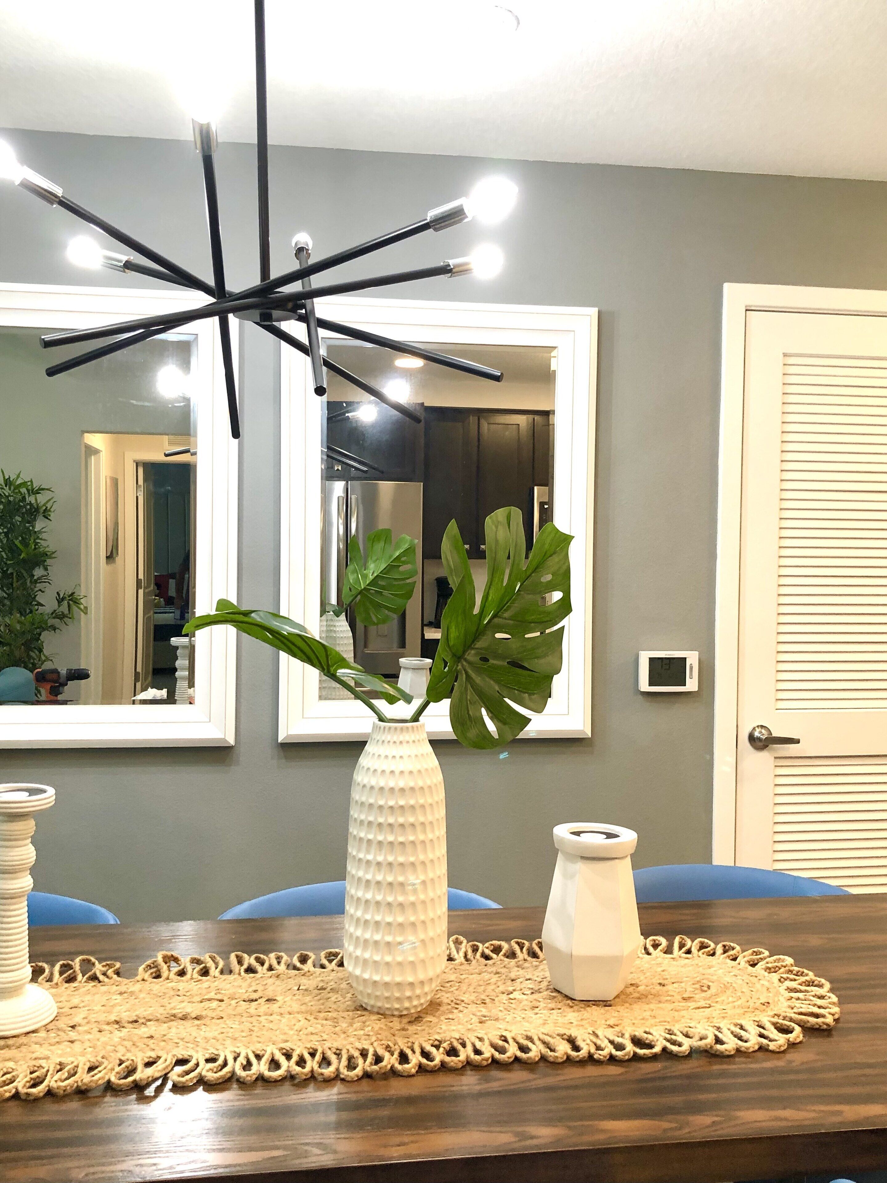 Un coin repas comprenant une table, un vase blanc à texture particulière agrémenté d’une plante, et un luminaire suspendu au design moderne.