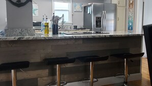 A modern kitchen with a central island, bar stools, stainless steel appliances, and a wooden floor.