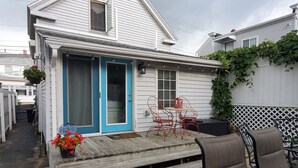 A small house with a blue door, a patio with outdoor furniture, and a garden with red flowers.
