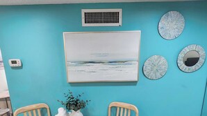 Un comedor con una mesa redonda de madera, dos sillas, un florero con planta y un respiradero en la pared.
