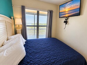 A hotel room with a bed, a television mounted on the wall, and a window with blinds.