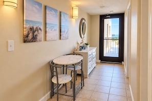A hallway with a dining area featuring a marble table and chairs, a white cabinet, and wall-mounted artwork. - Coastal Luxe | Buena Vista Four Oh Two (North Myrtle Beach)
