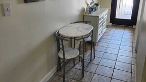 Un pasillo con suelo de baldosas, una pequeña mesa redonda con una silla, un espejo y obras de arte en la pared.
