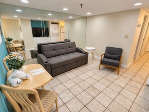 A compact living space with a sofa, a chair, a small table with a plant, and a television in the background.