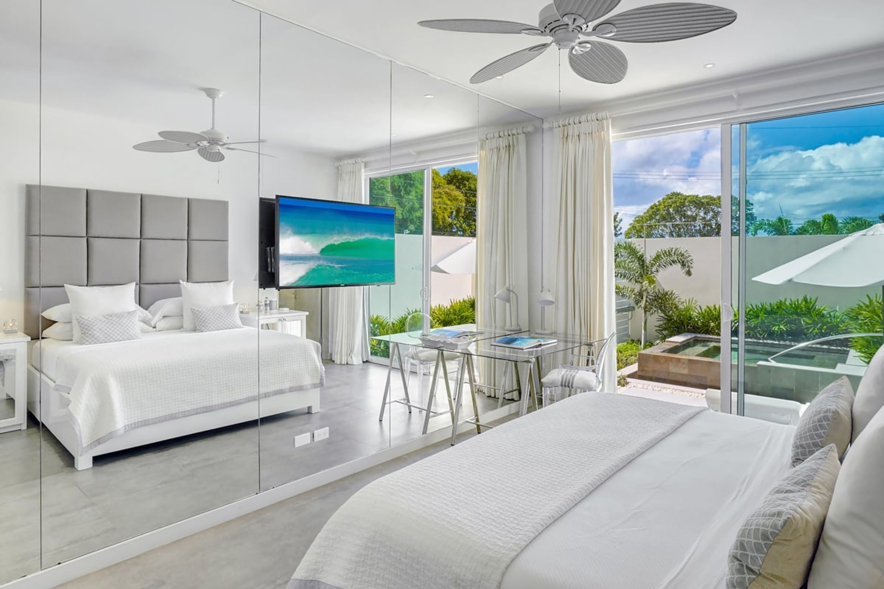 A modern hotel room with a large bed, a desk, and a balcony with a view of greenery.