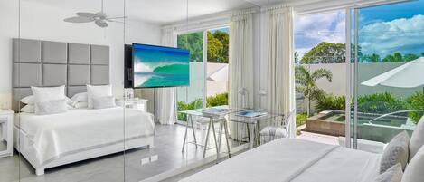 A modern hotel room with a large bed, a desk, and a balcony with a view of greenery.