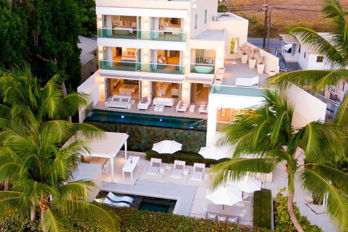 A multi-story modern house with a pool, outdoor seating, and lush greenery.