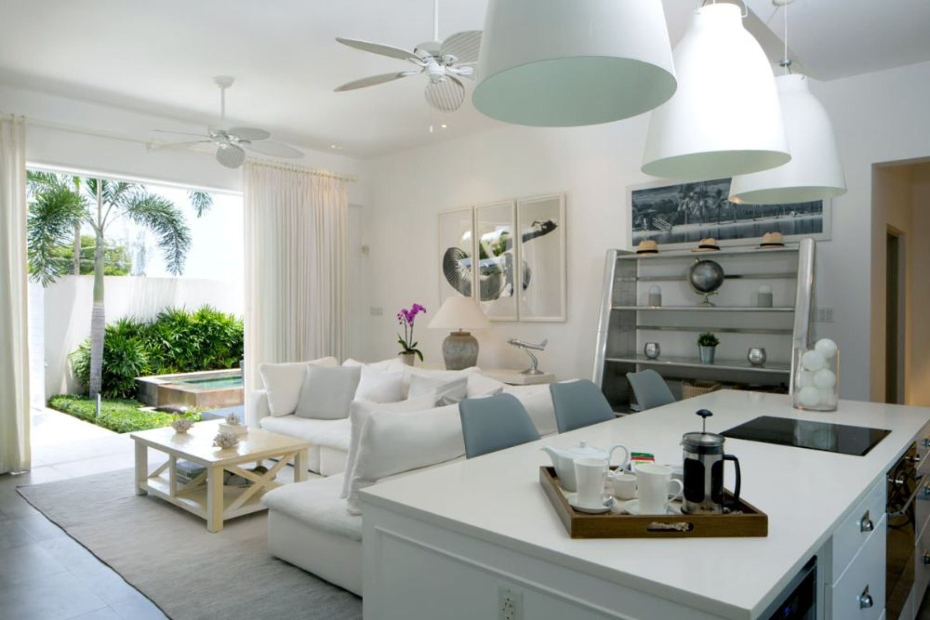 A modern living room with a white sofa, coffee table, and a kitchen island with a tray of breakfast items.