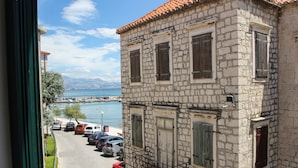 A stone building with multiple windows and a balcony, overlooking a marina with parked cars and boats. - Modern apt in the Stone House in the Very Center (Kastela)