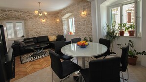 A living room with a stone wall, a round table with chairs, a sofa, and a television. - Modern apt in the Stone House in the Very Center (Kastela)