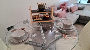 A modern living room with a glass table, white sofa, and a wooden side table with a teapot and snacks. - 2 Bed Woodland Retreat - Garden & Free Parking (Keighley)