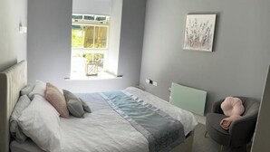 A bedroom with a bed, a chair, a window, and a wall-mounted picture. - 2 Bed Woodland Retreat - Garden & Free Parking (Keighley)