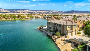 A residential area with houses near a body of water, a clear sky, and mountains in the background. - Lakefront Dream: Misters and The Best Corner Lot on the Lake! EV! (Indio)