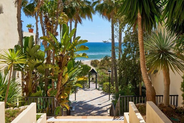 A pathway leading to a beach with palm trees and a gazebo. - Sun all day double wide balcony with panoramic sea view (Marbella)