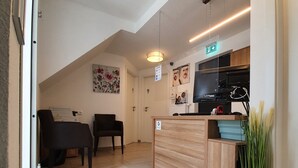 A modern interior with a reception desk, two black chairs, a wooden counter, a painting, and a potted plant. - Gap Hotel  (Langwedel)