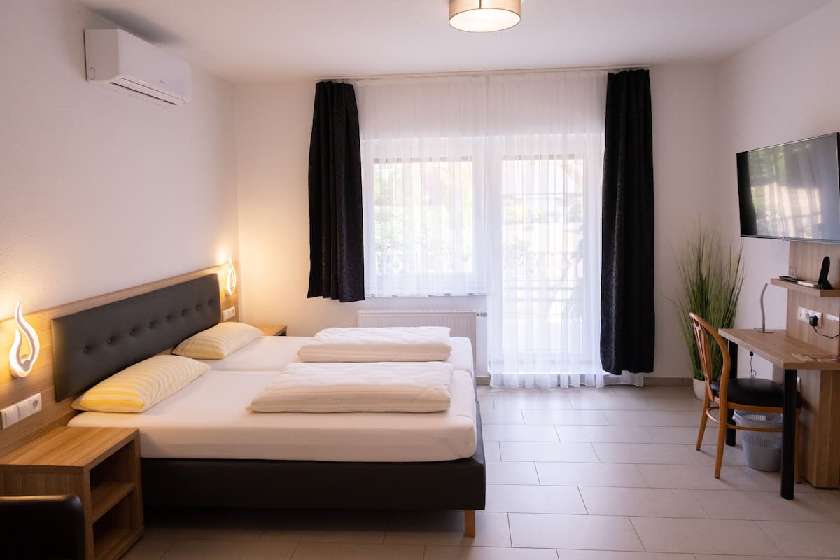 Habitación de hotel con cama, mesitas de noche, escritorio, silla, televisor y una planta en maceta.