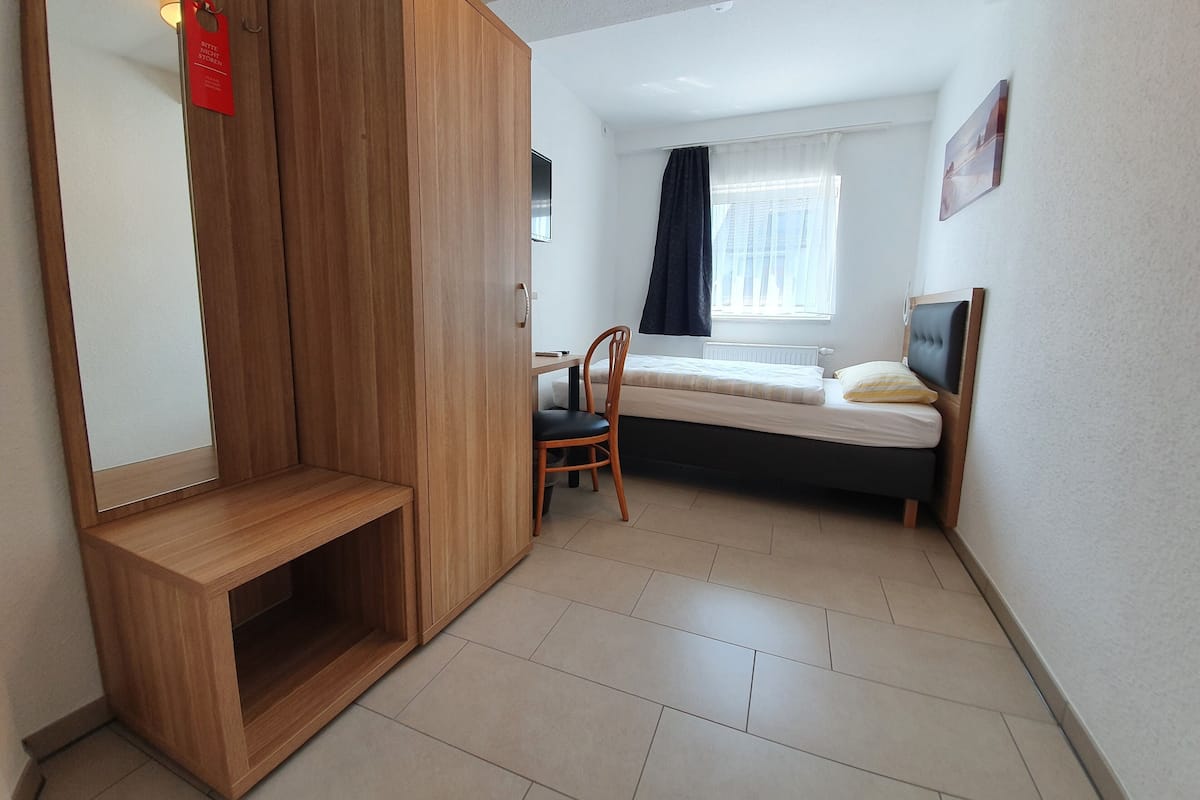 Una habitación pequeña con cama, una silla, un armario de madera y una mesita.