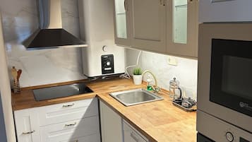 Cocina compacta con armarios blancos, un lavamanos de acero inoxidable, horno empotrado y encimera de madera.