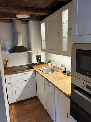 Cocina compacta con armarios blancos, un lavamanos de acero inoxidable, horno empotrado y encimera de madera.