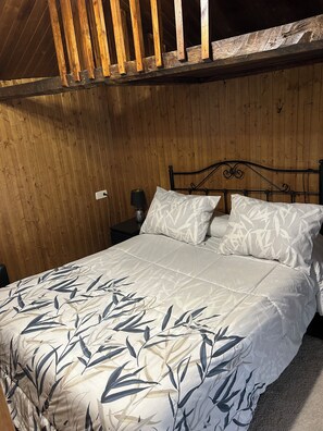 A bedroom with a wooden ceiling, a metal bed frame, and a bed with a leaf-patterned bedspread.