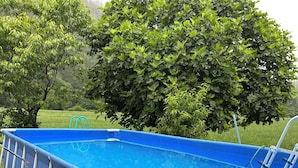 Ein blauer Aufstellpool mit einer Leiter, umgeben von einer Rasenfläche und Bäumen.