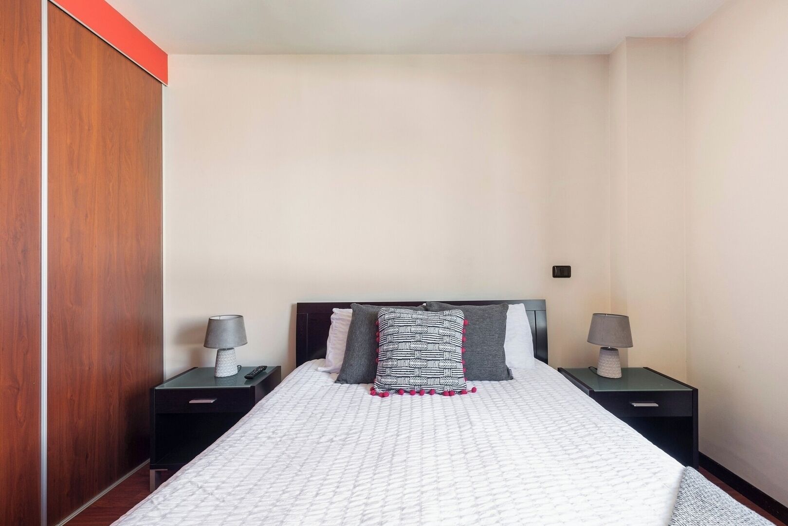 A bedroom with a bed, two nightstands, a wardrobe, and a wall-mounted light switch.