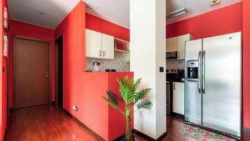 A compact kitchen with red walls, a wooden floor, a refrigerator, and a potted plant.