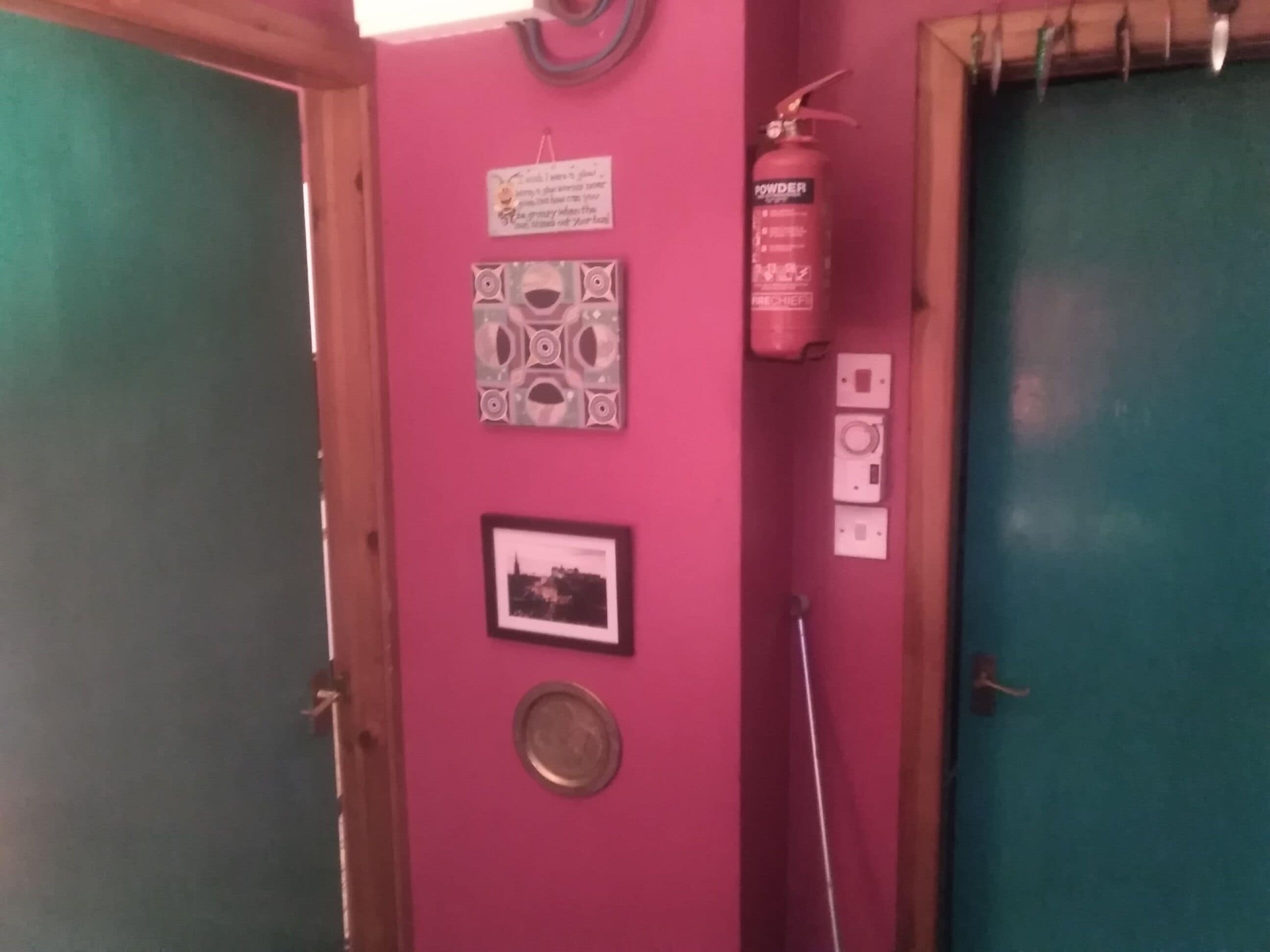 Eine rosa Wand mit einem Feuerlöscher, einem gerahmten Bild und einer Dekoteller.