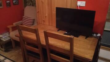 Een houten eettafel met twee stoelen, een televisie en een stopcontact aan de muur.