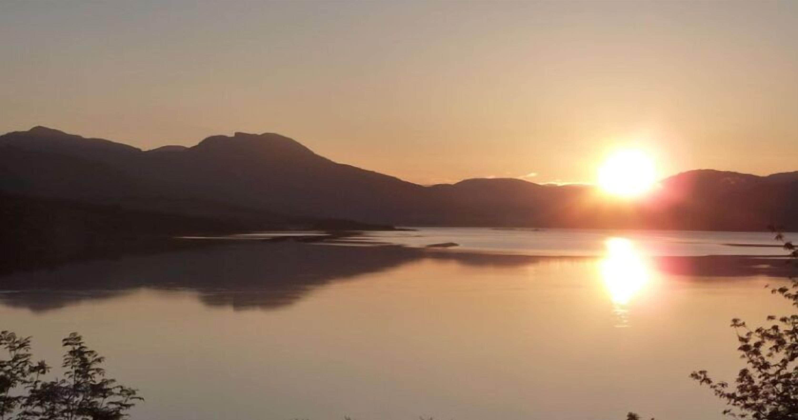 Un lago tranquilo al atardecer con montañas al fondo.