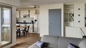 A modern apartment with a dining area, kitchenette, and a grey sofa with patterned cushions. - Appt 1ère Ligne 2 Terrasses 3 Chambres Accés Direct à la Plage (Canet-en-Roussillon)