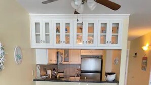 A dining area with a glass table surrounded by chairs, a ceiling fan, and white cabinets above.