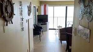 A hallway with a TV, chairs, and a dining area with a table and chairs.