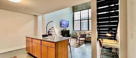 A modern kitchen with a central island, a dining area with a table and chairs, and a living space with a sofa and TV.