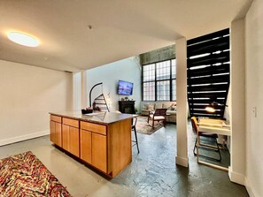 Een moderne keuken met een centraal eiland, een eethoek met een tafel en stoelen, en een woonruimte met een bank en televisie.