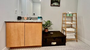 Un bagno con un armadietto in legno, un lavandino, uno specchio, un quadro appeso al muro, una pianta in vaso e un porta asciugamani.
