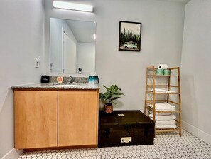 A bathroom with a wooden cabinet, a sink, a mirror, a framed picture on the wall, a potted plant, and a towel rack.