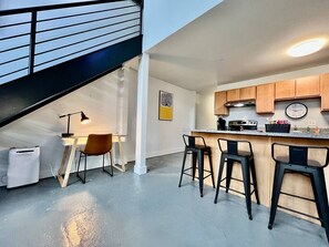 A modern kitchen with a bar area, a dining table with chairs, and a staircase.