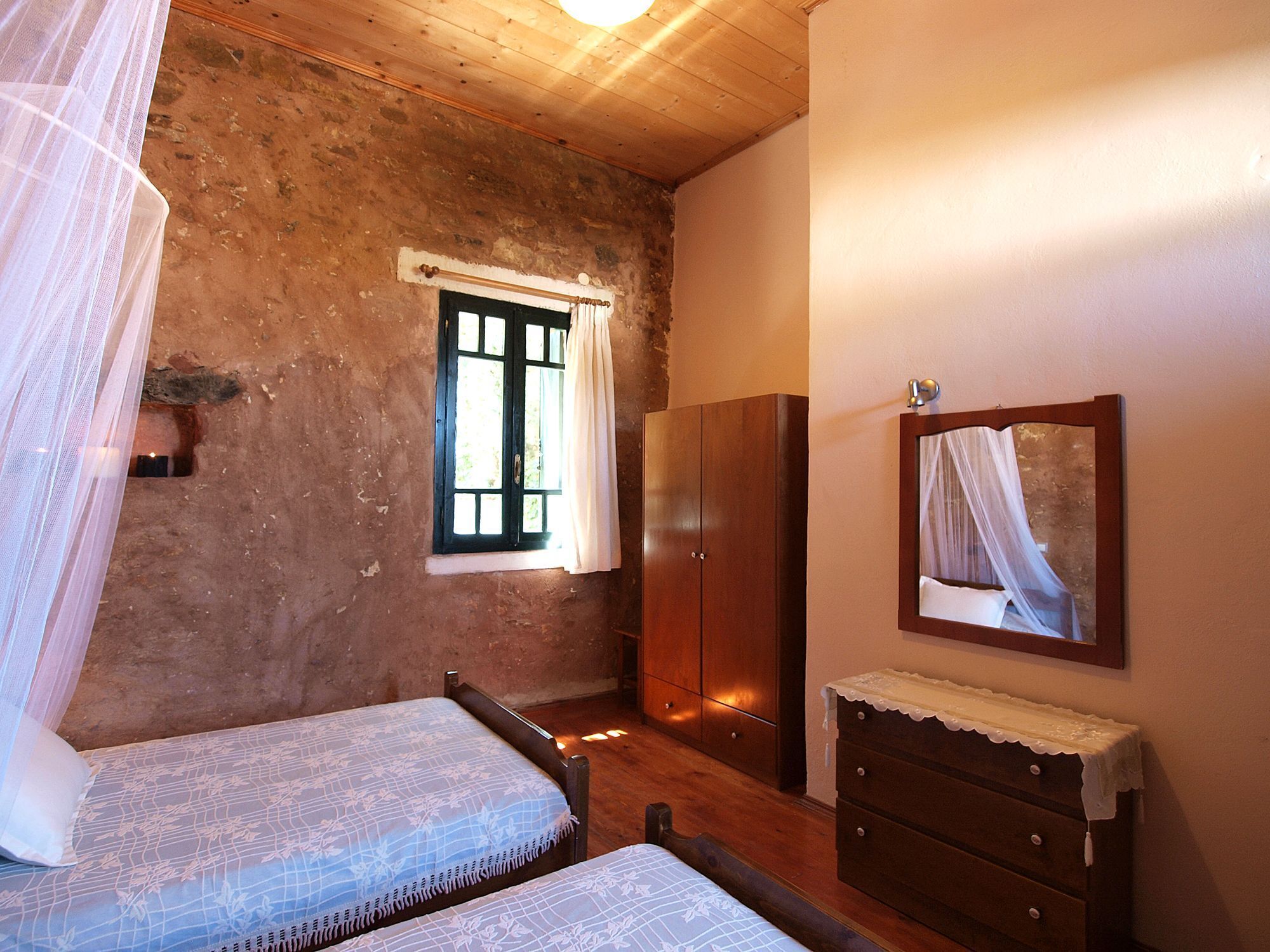 Une chambre rustique comprenant un lit, une armoire, un miroir et une fenêtre avec des rideaux.