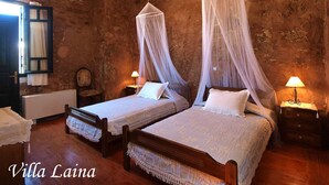 Una habitación rústica con dos camas, cada una con dosel, una silla de madera, una mesita y una lámpara.