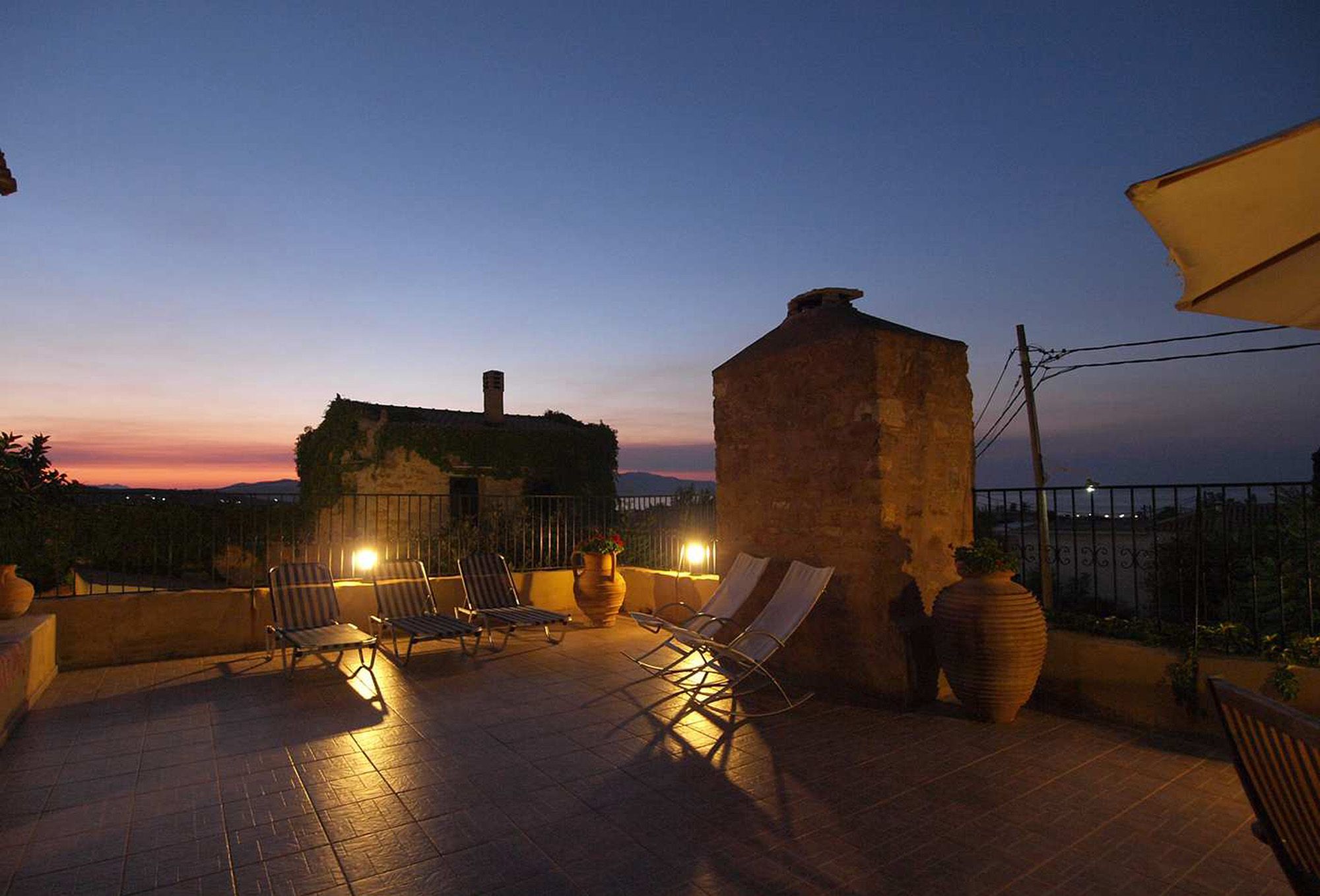 Une terrasse avec des fauteuils et un grand vase, le tout mis en valeur par le décor d’un coucher de soleil.
