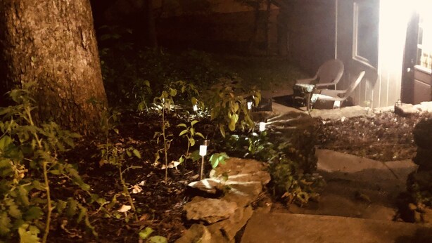 Ein Außenbereich bei Nacht mit einem Kiesweg, Pflanzen und einem Tisch mit Stühlen.