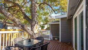 Une terrasse avec une table et des chaises, un grand arbre et une maison avec une balustrade blanche et une porte de garage.