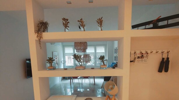Ein mehrgeschossiges Interieur mit einem zentralen Tisch, Regalen mit Dekoration und einer Treppe.