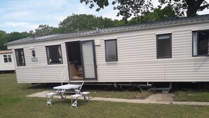 A mobile home with a sliding door, a small patio with a table and chairs, and a grassy yard. - 3-bedroom Caravan at Thorness bay (Cowes)