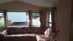A cozy RV interior with a sectional sofa, large windows, and a view of the backyard. - 3-bedroom Caravan at Thorness bay (Cowes)